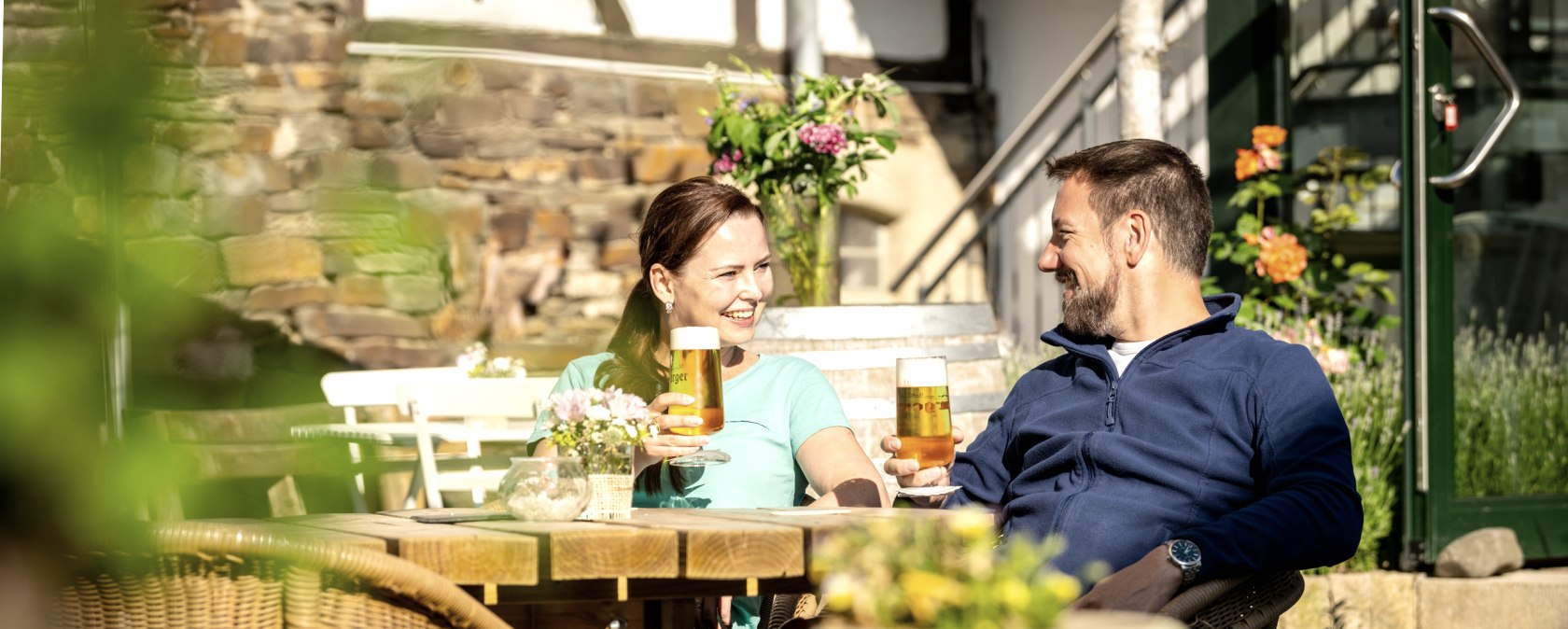 Eien Frau udn ein Mann mit einem Glas Bier sitzen in einem Biergarten und prosten sich zu