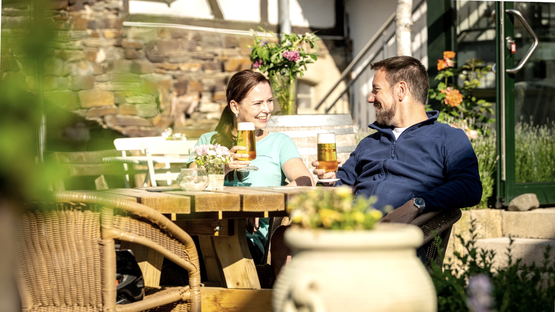 Eien Frau udn ein Mann mit einem Glas Bier sitzen in einem Biergarten und prosten sich zu